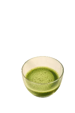 A clear glass bowl filled with bright green matcha tea, set on a warm beige surface with soft window shadow patterns.
